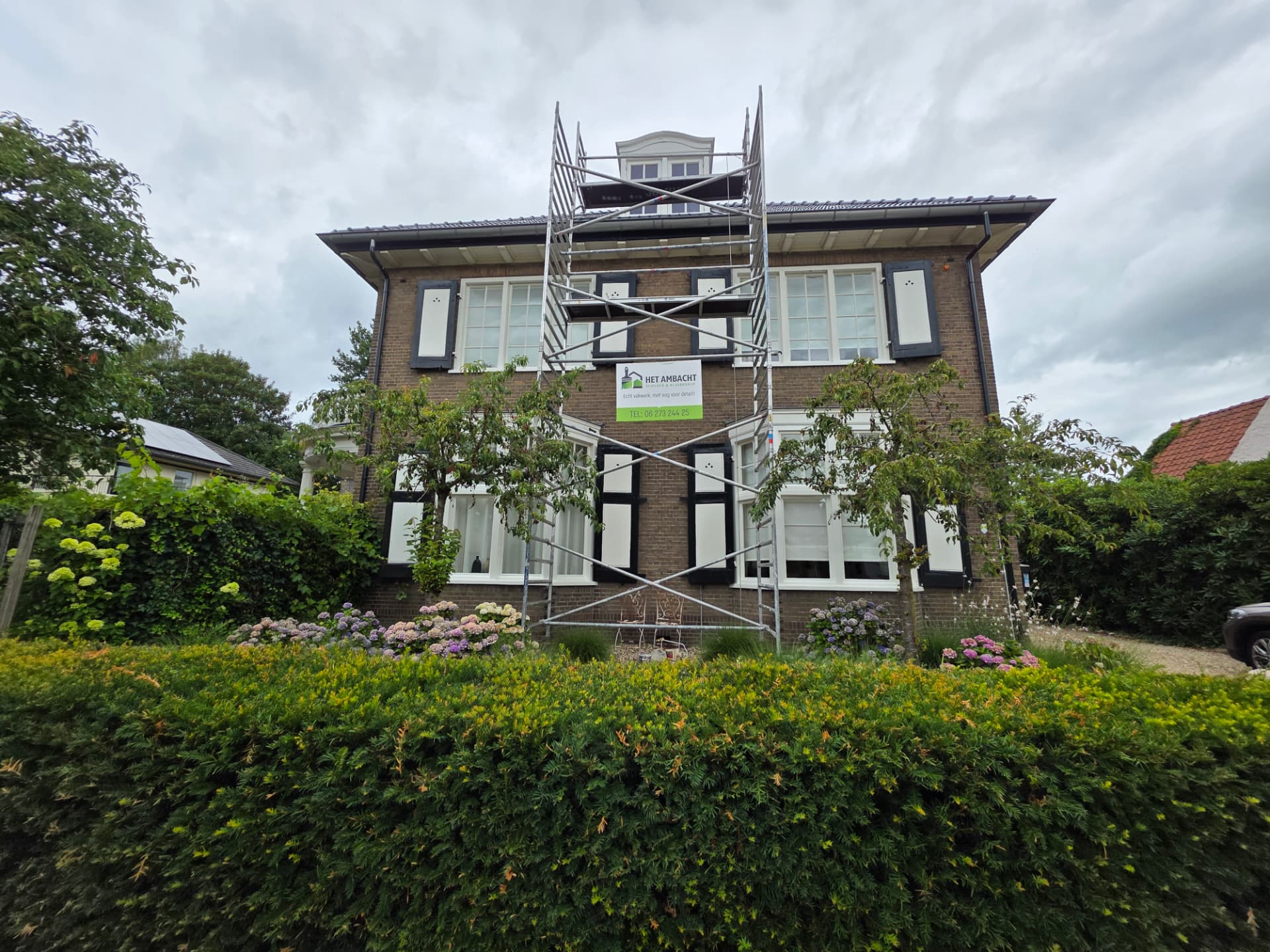 Steiger met bedrijfsbord voor de woning tijdens de schilderwerkzaamheden