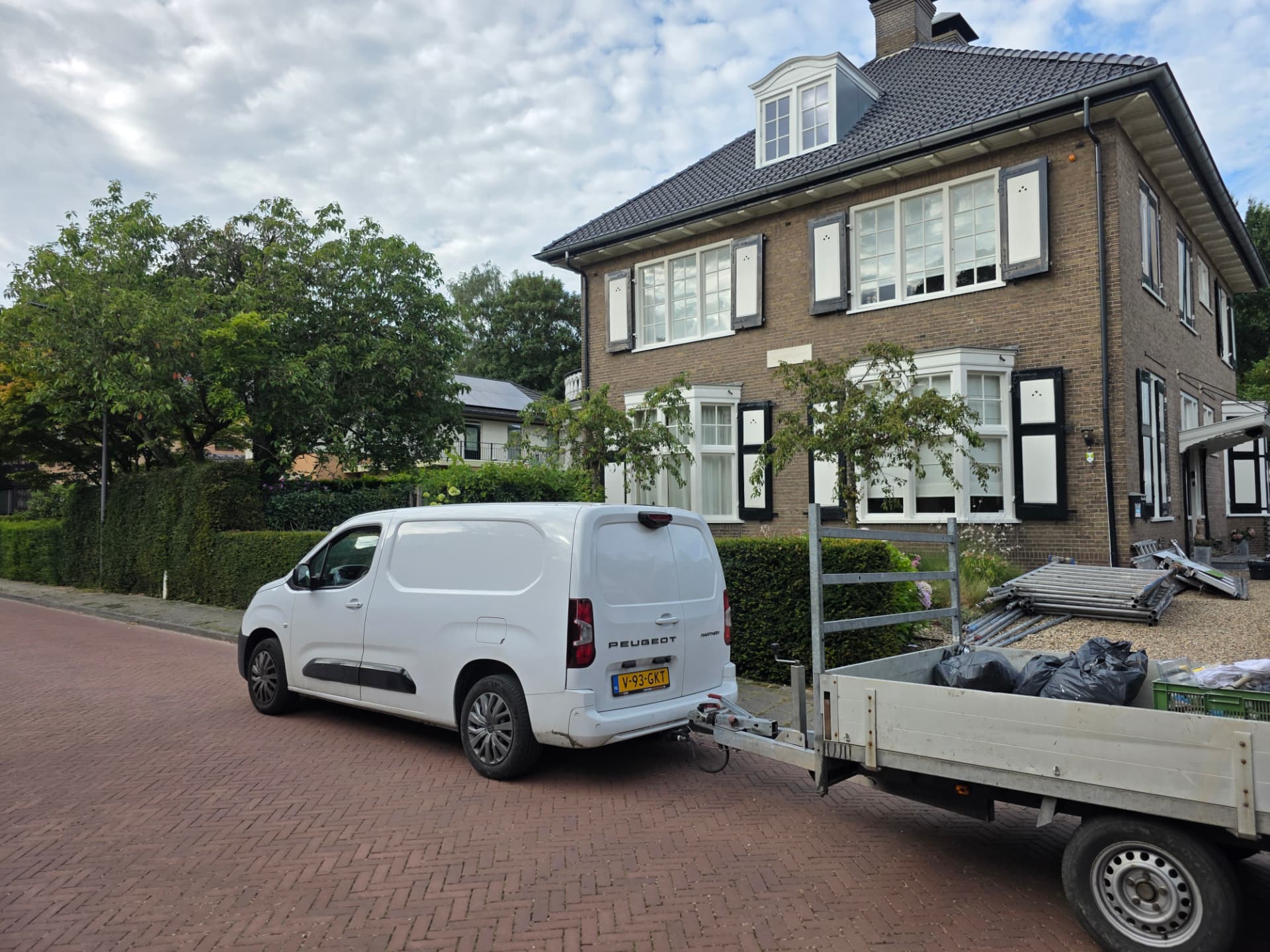 Ruim straatbeeld van de onderhouden woning met werkbus en aanhanger