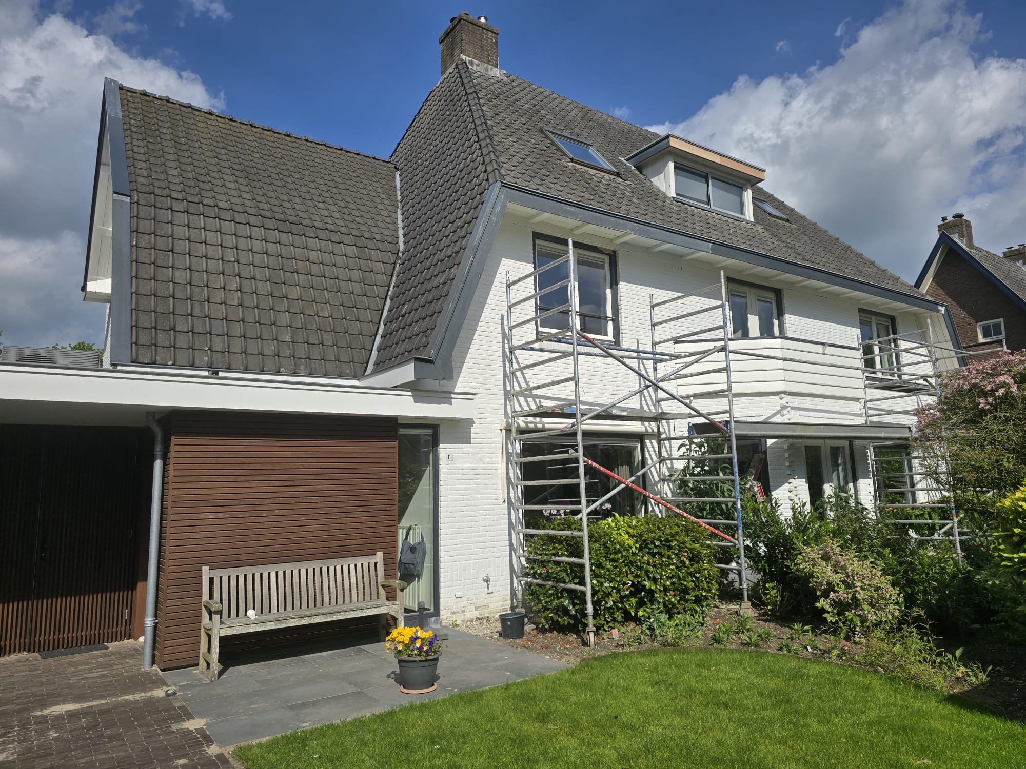 Zijaanzicht van het woonhuis tijdens schilderwerk aan kozijnen en dakranden