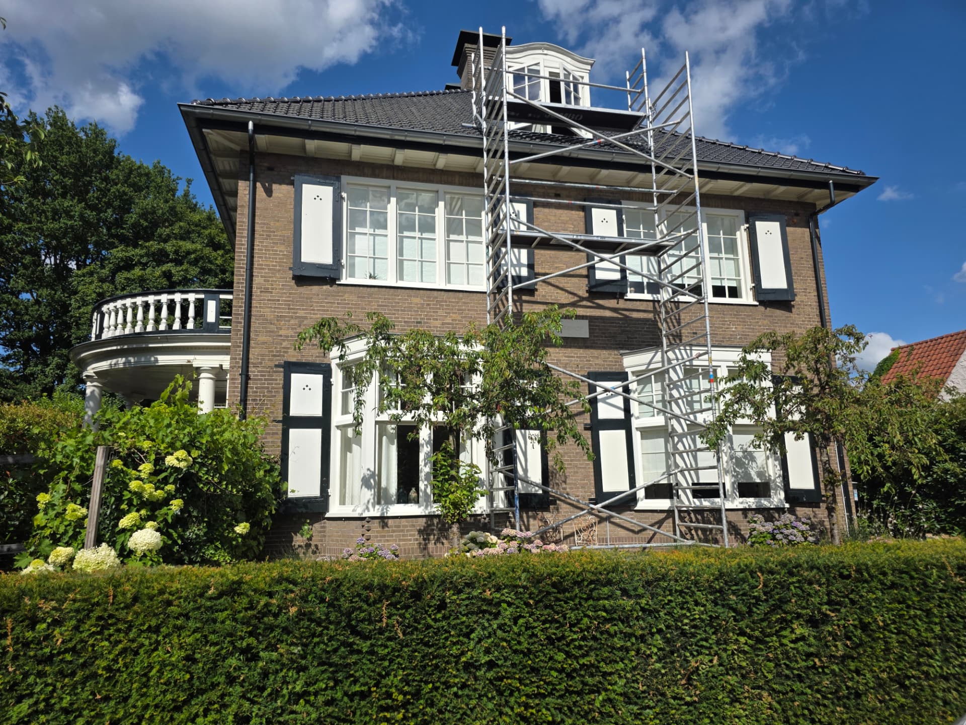 Zonnig vooraanzicht van de woning met steiger tijdens het onderhoudsschilderwerk